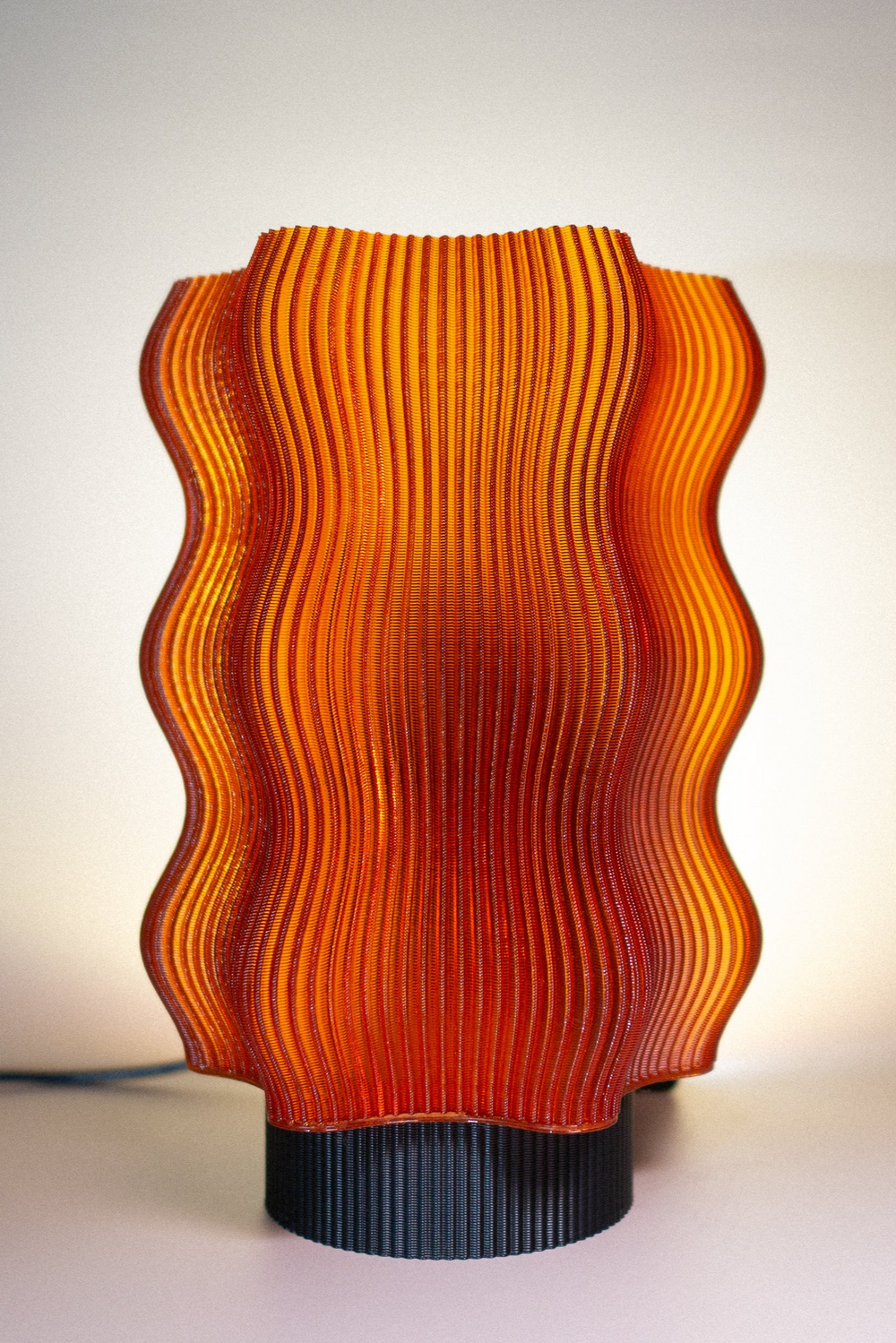 The OrijaDesign Reef Table Lamp features a wavy, ribbed orange design on a black base, softly glowing—an ocean-inspired accent perfect for coral reef-themed decor.