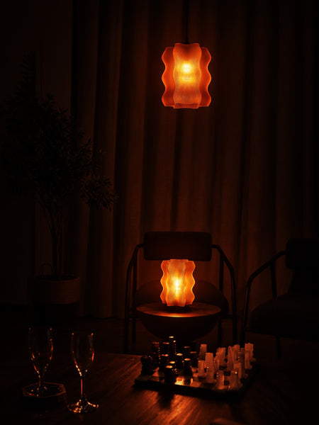 A dimly lit room features two Reef Pendant lights from My Store casting an atmospheric glow; a chessboard is set in the foreground while empty chairs and glasses contribute to the quiet ambiance.