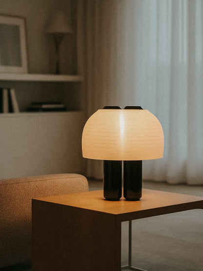 The OrijaDesign Nami Table Lamp, featuring a pleated lampshade, rests on a wooden side table in a softly lit minimalist living room, capturing the elegance of Japanese paper lanterns.