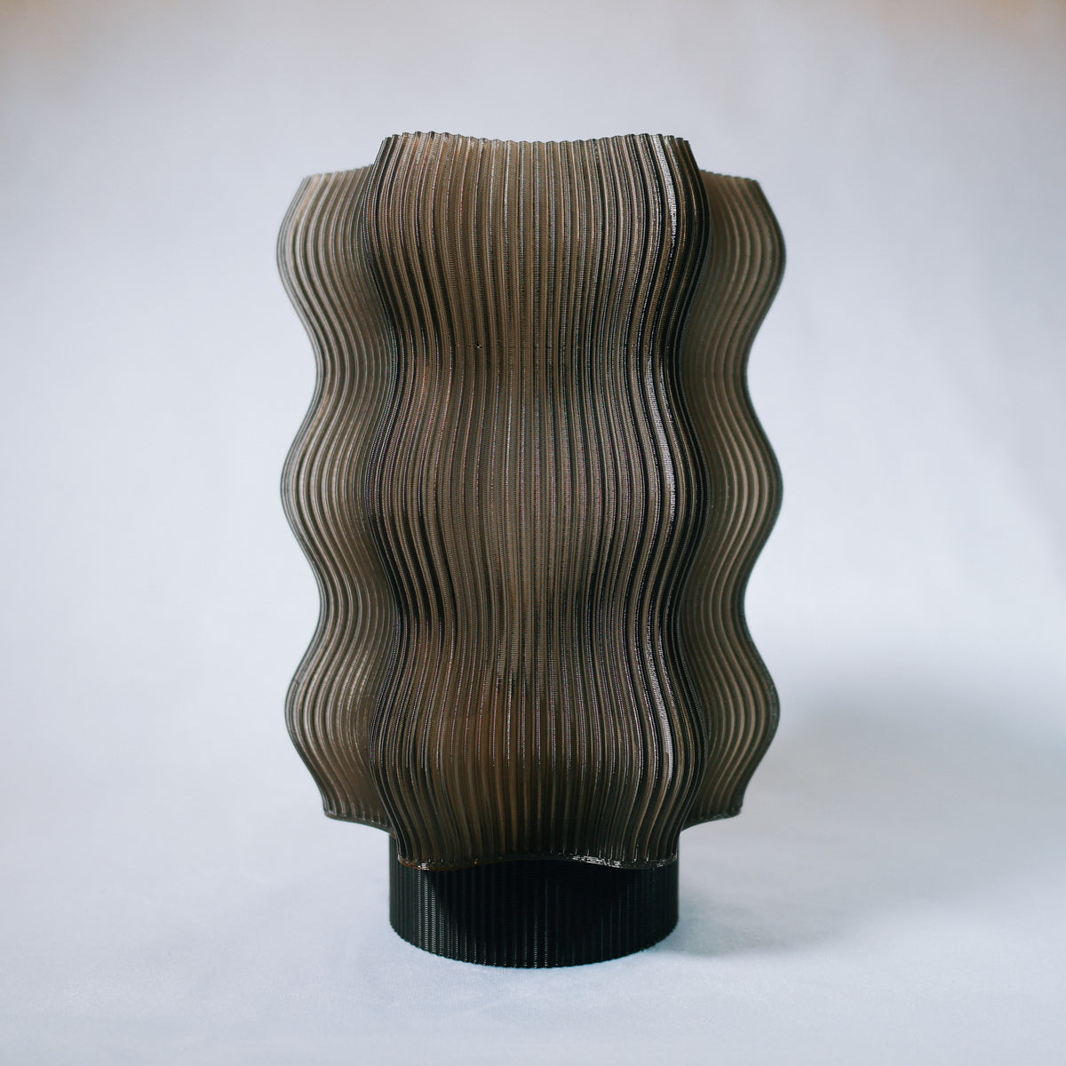 The Reef Table Lamp by OrijaDesign features undulating vertical ridges reminiscent of coral reefs and a translucent smoky brown finish, set against a plain light background.