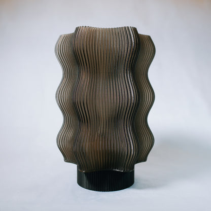 The Reef Table Lamp by OrijaDesign features undulating vertical ridges reminiscent of coral reefs and a translucent smoky brown finish, set against a plain light background.