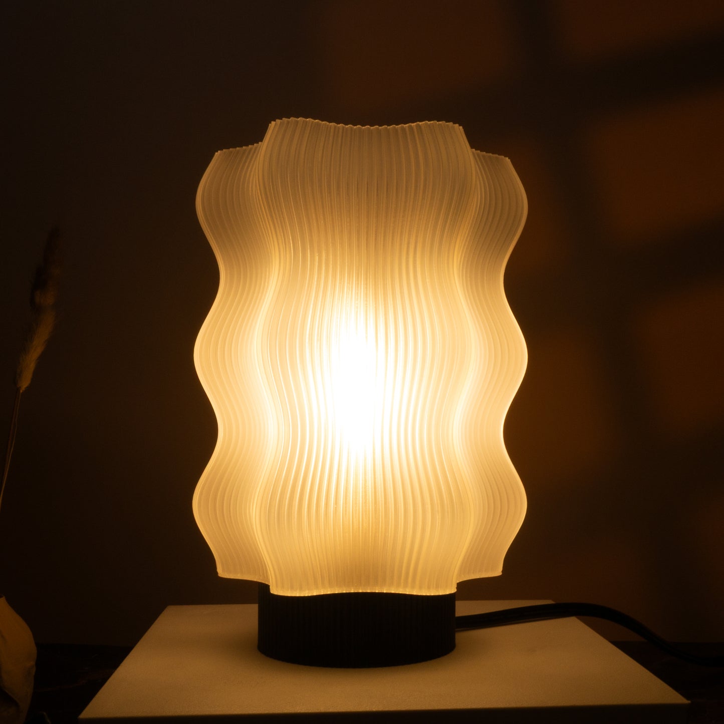 The Reef Table Lamp by OrijaDesign features a wavy, textured white shade that brings ocean-inspired decor and a warm, soft glow to any dimly lit room.
