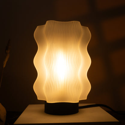The Reef Table Lamp by OrijaDesign features a wavy, textured white shade that brings ocean-inspired decor and a warm, soft glow to any dimly lit room.