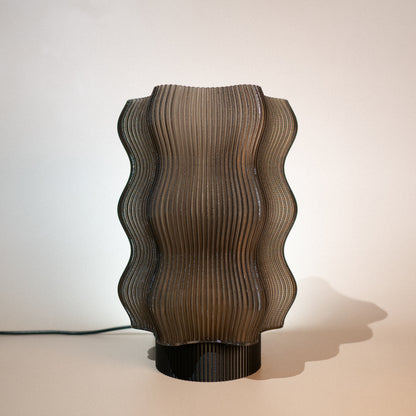 The Reef Table Lamp (Seconds) by OrijaDesign features a sculptural design with a wavy, ribbed brown shade and black base, evoking coral reefs—ideal for adding subtle, modern elegance to your decor.