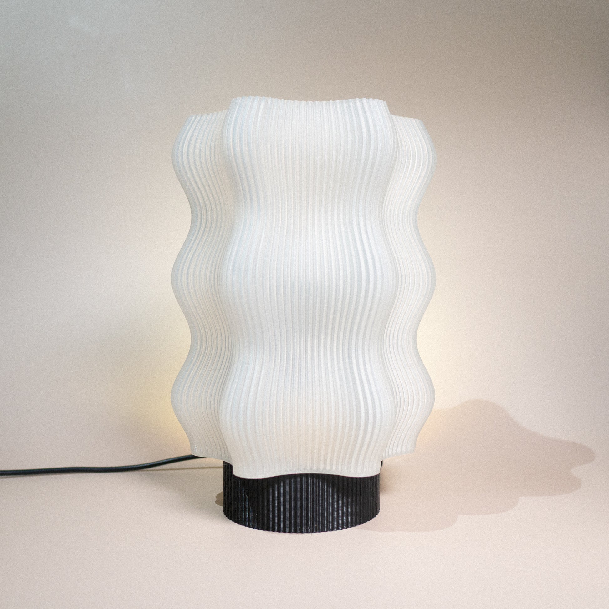 The Reef Table Lamp by OrijaDesign features a wavy, ribbed white shade and a black cylindrical base, capturing the gentle curves of coral reefs—an elegant addition to any ocean-themed decor.